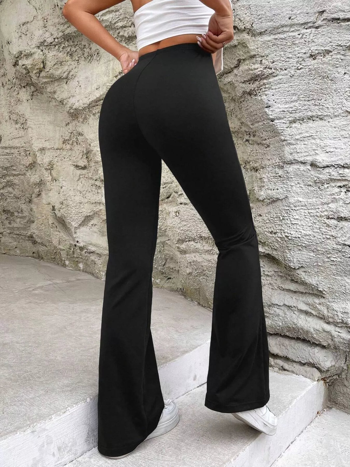 Rear three-quarter view of black flare pants worn on stone steps, showing the fitted seat and wide hems.