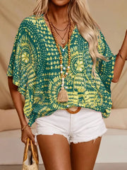Green medallion-print blouse shown with one half sleeve lifted and tassel neck ties hanging down.