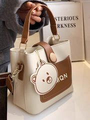 Side view of ivory and brown bucket crossbody bag with bear charm and detachable strap
