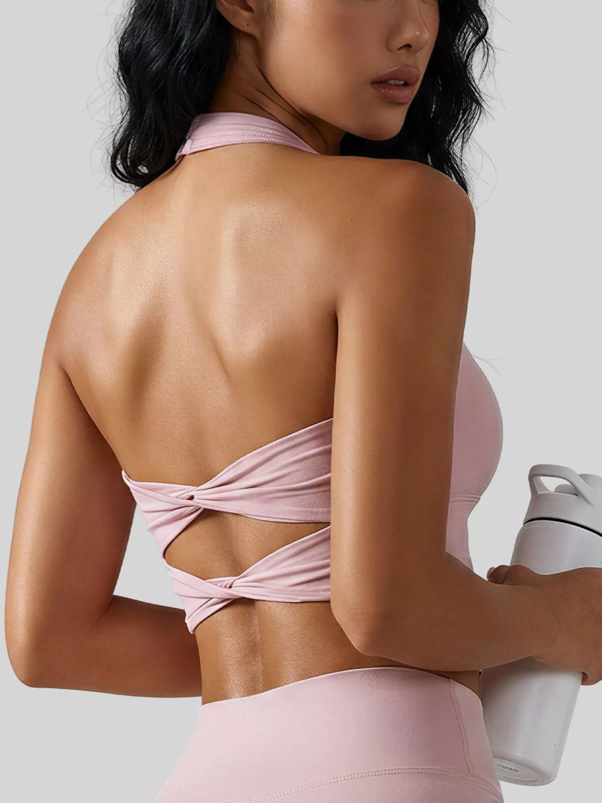 Rear three-quarter view of a pale pink halter active bra with two twisted back bands.