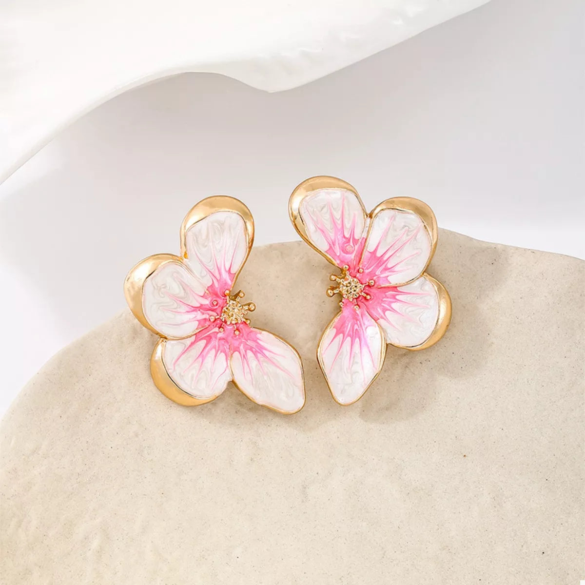 Pair of pink-and-white flower studs resting on a pale stone
