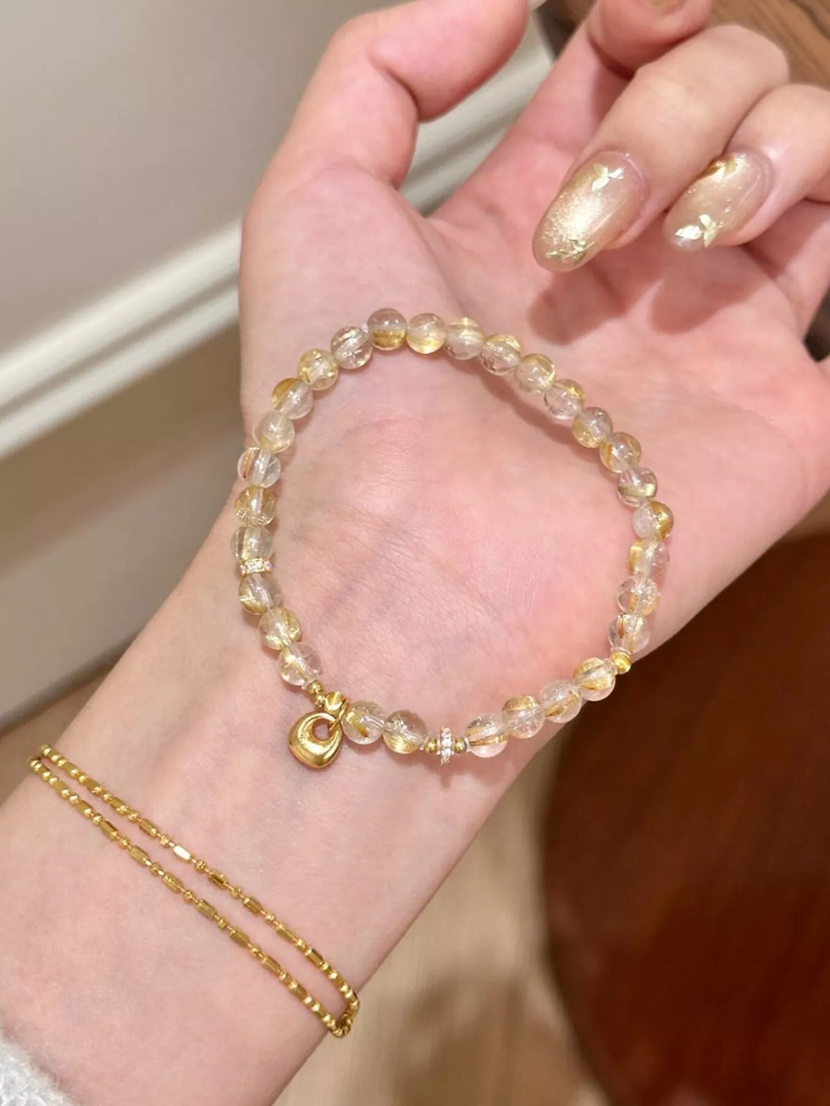 Gold-tone beaded charm bracelet looped across a palm to show its clasp and charms.