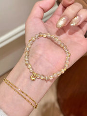 Gold-tone beaded charm bracelet looped across a palm to show its clasp and charms.
