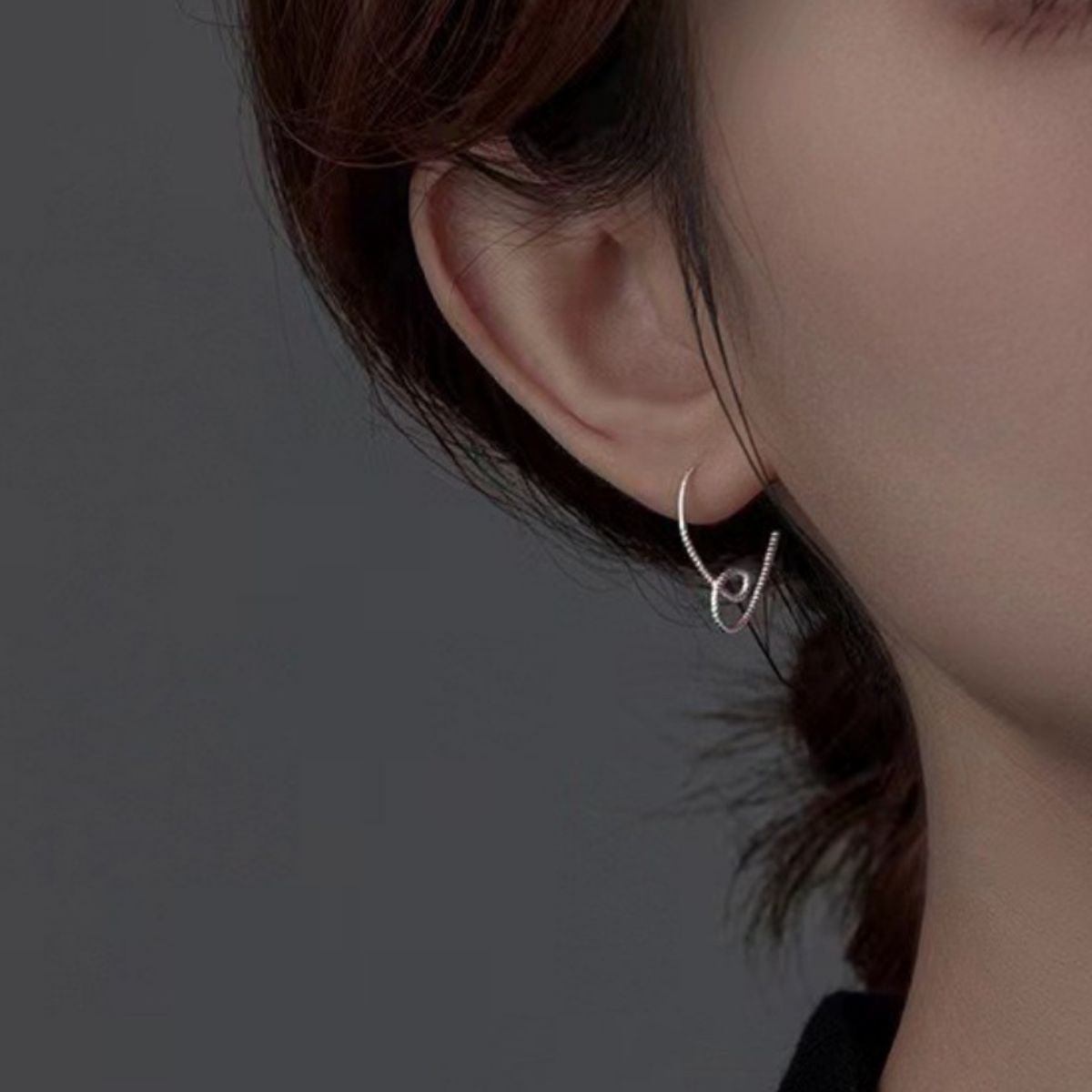 Silver heart-shaped drop earring worn on an ear, front angle