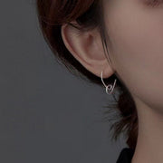 Silver heart-shaped drop earring worn on an ear, front angle
