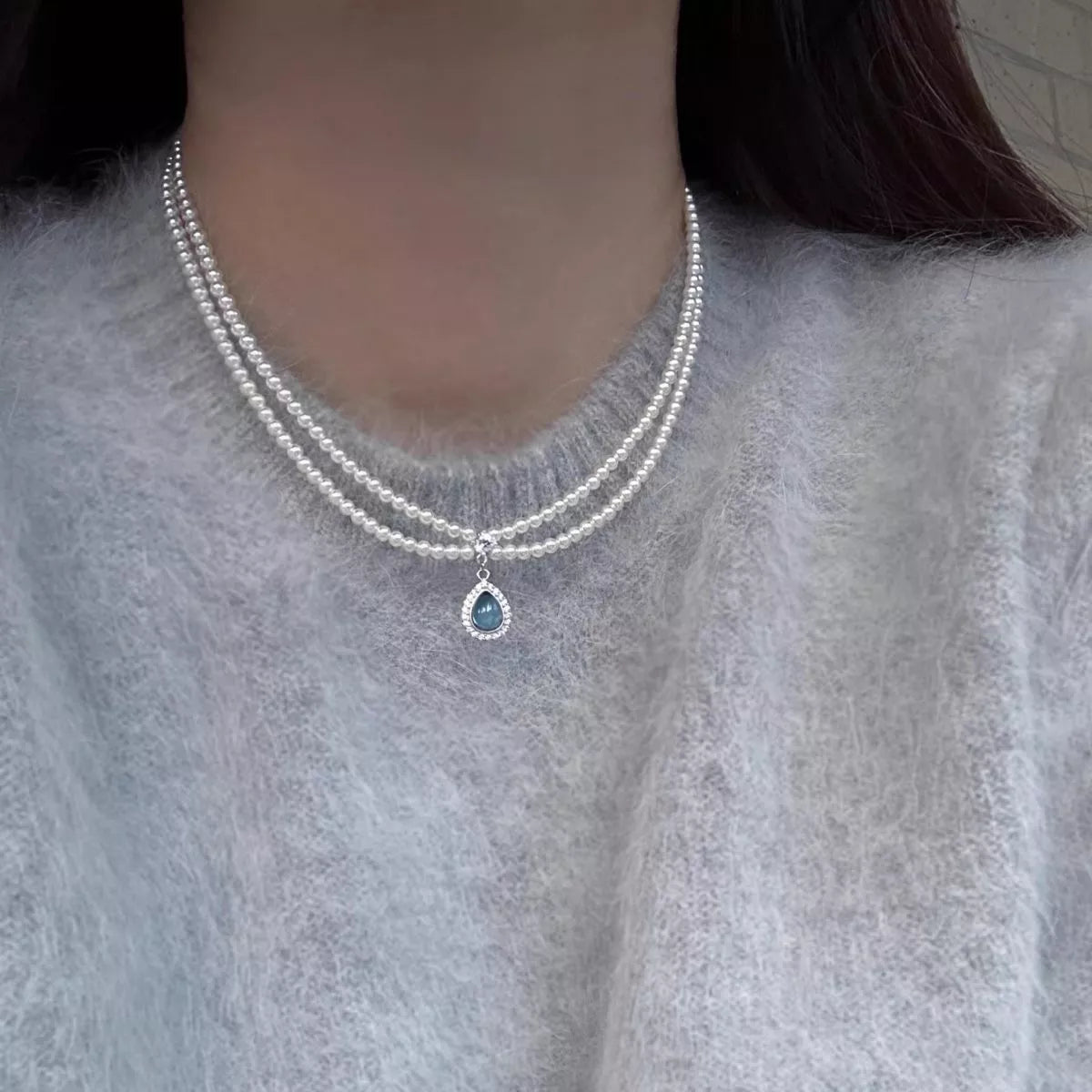 Double-layer pearl necklace with blue teardrop pendant worn at the neckline