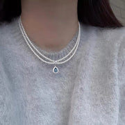 Double-layer pearl necklace with blue teardrop pendant worn at the neckline