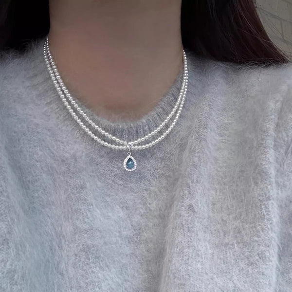 Double-layer pearl necklace with blue teardrop pendant worn at the neckline