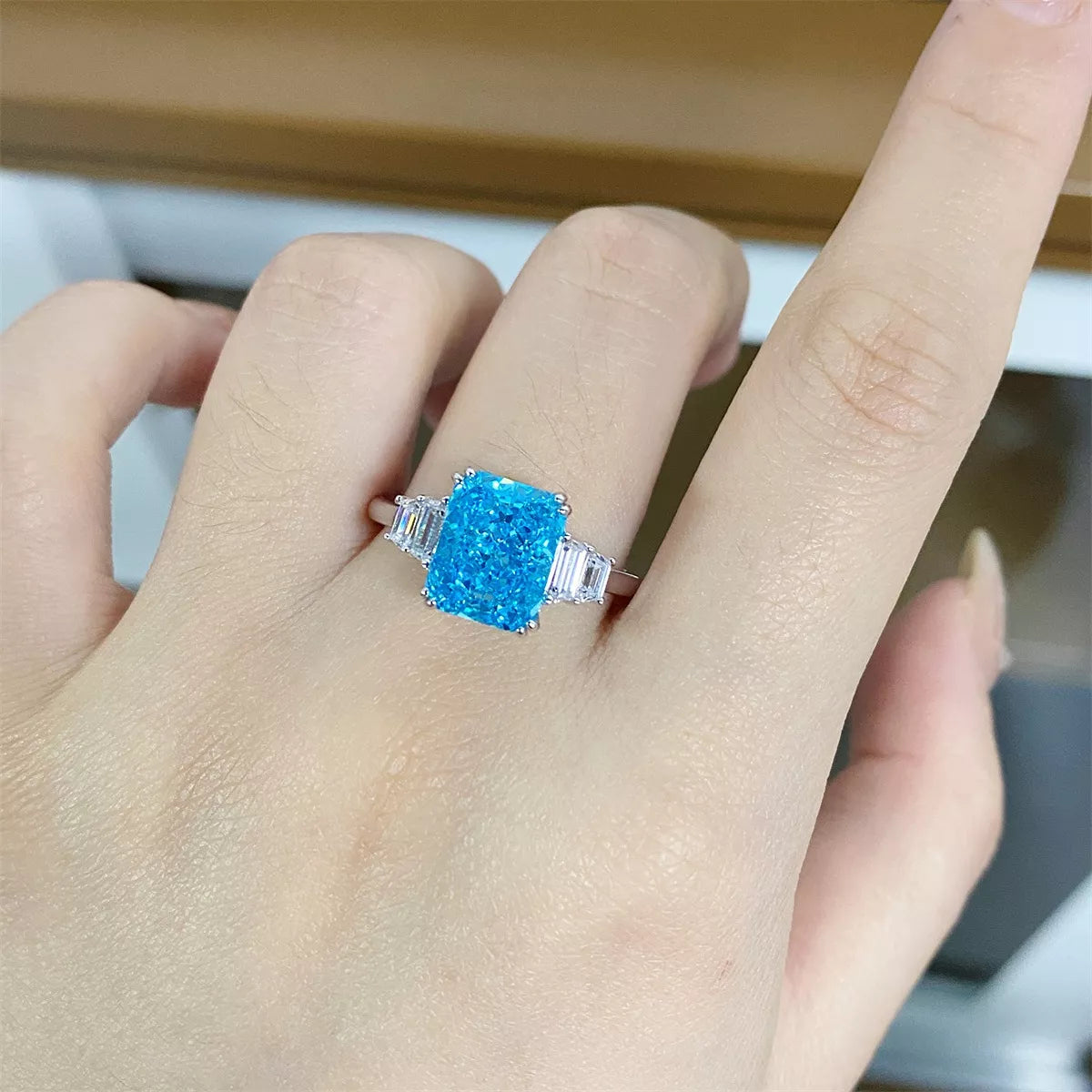 Close view of a pastel blue rectangular zircon ring worn on a finger