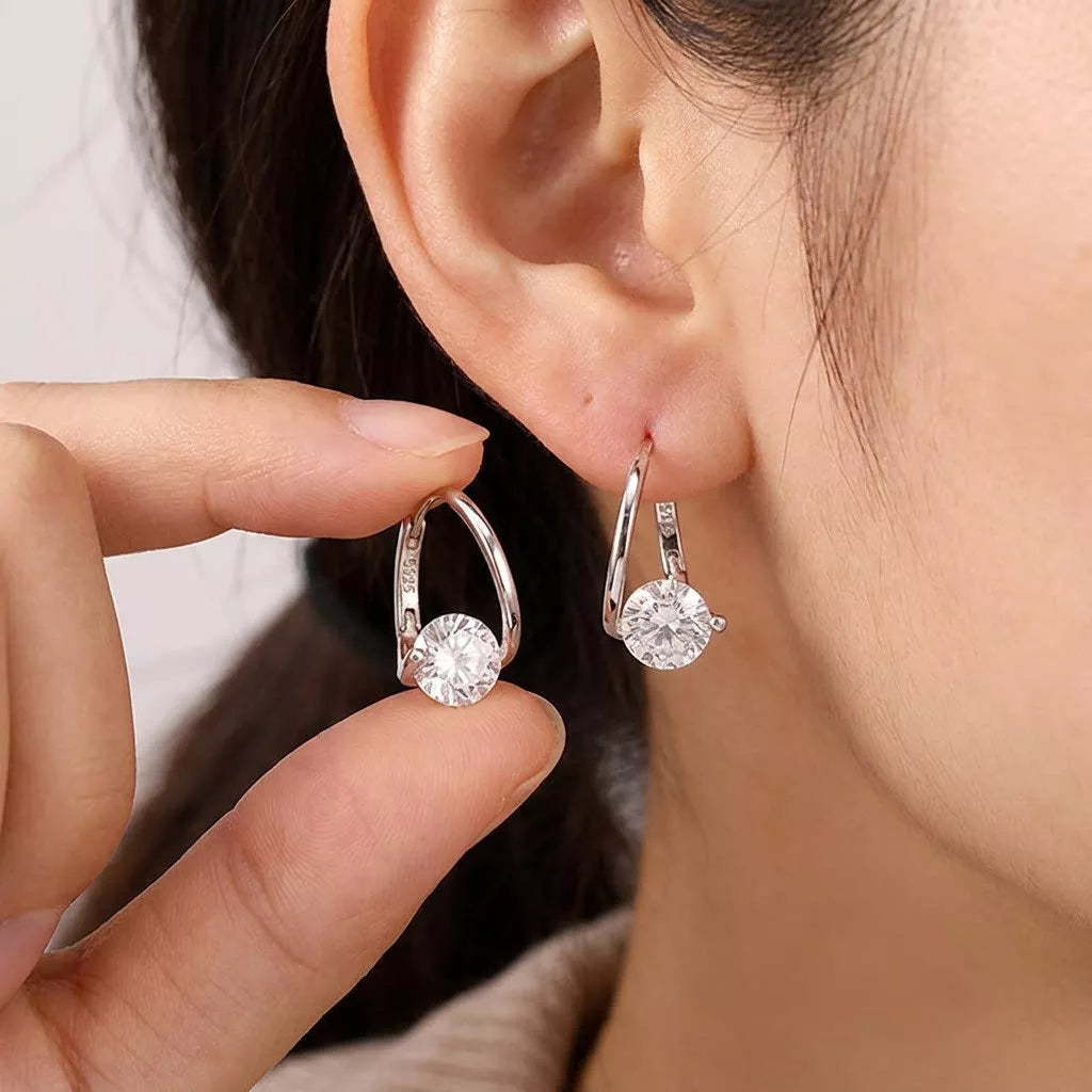 Gold-tone open hoop earrings with clear round stones worn on an ear