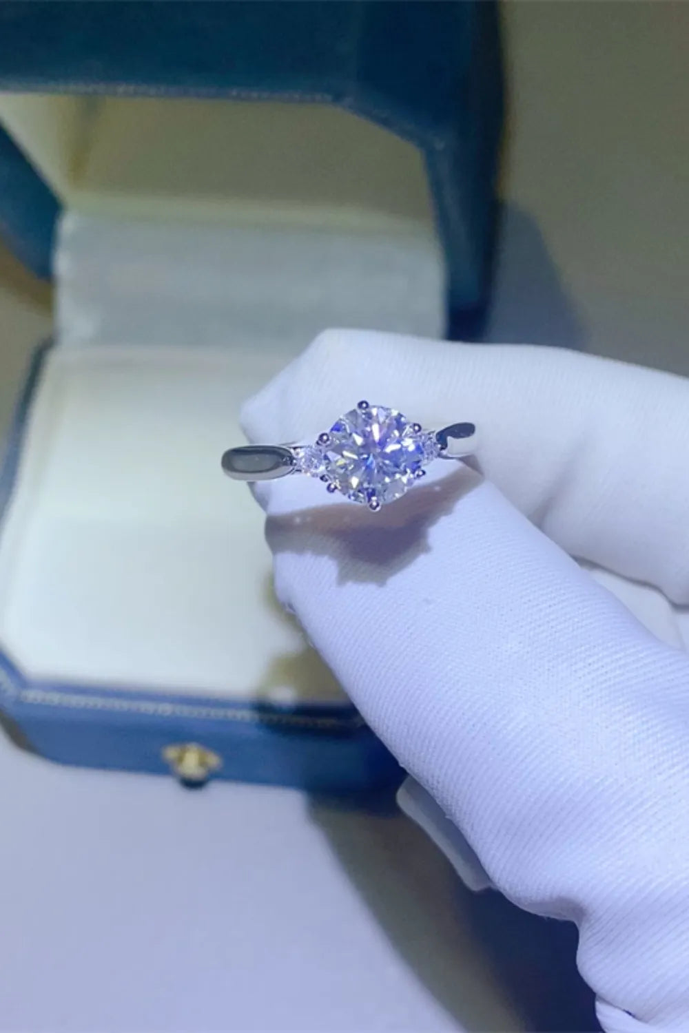 Purple-stone ring held in a gloved hand beside a ring box