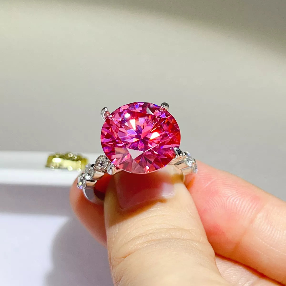 Front view of hot pink round stone ring held between fingers