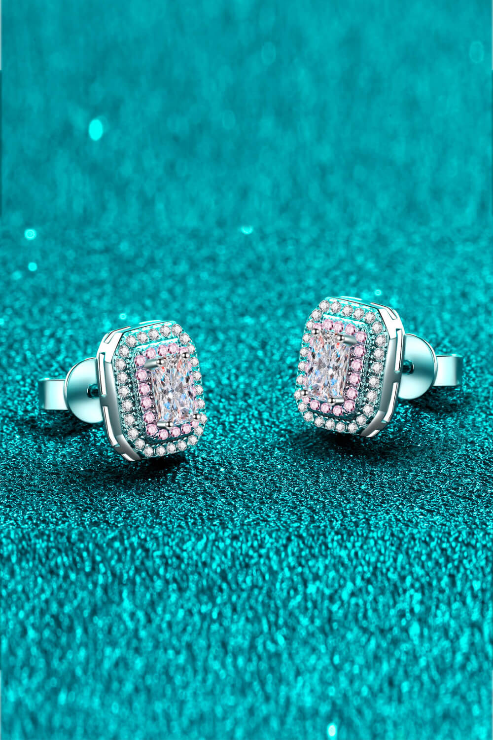 Angled view of pink-bordered rectangular stud earrings with butterfly backs on teal