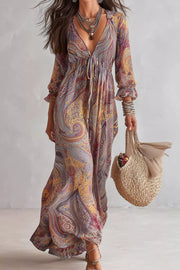 Full-length front view of a multicoloured paisley maxi dress with a tie neckline and long sleeves.