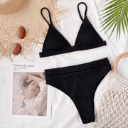 Black ribbed bikini set laid flat on white fabric with accessories