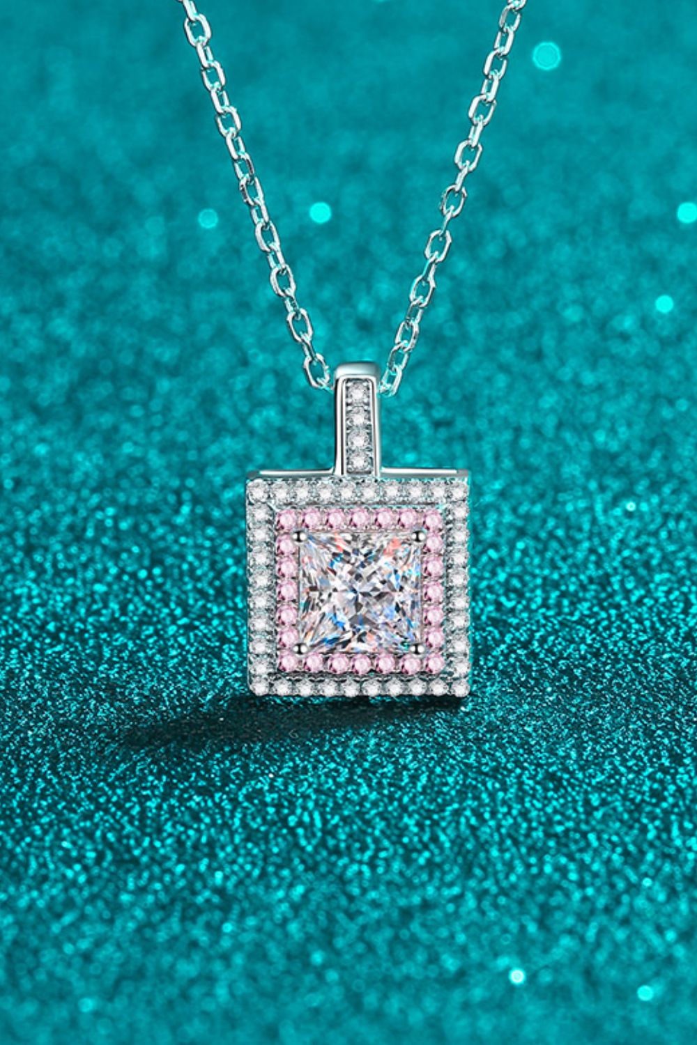 Square clear-stone pendant with pink border displayed on teal