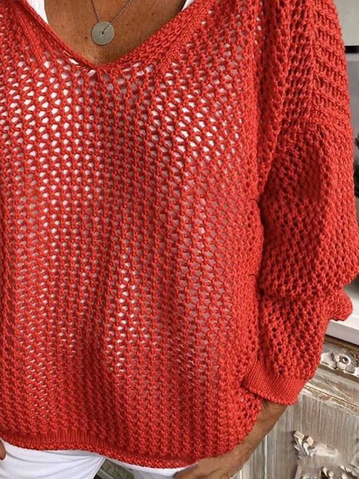 Red knit cover-up showing its loose lower front and long sleeves above white shorts.