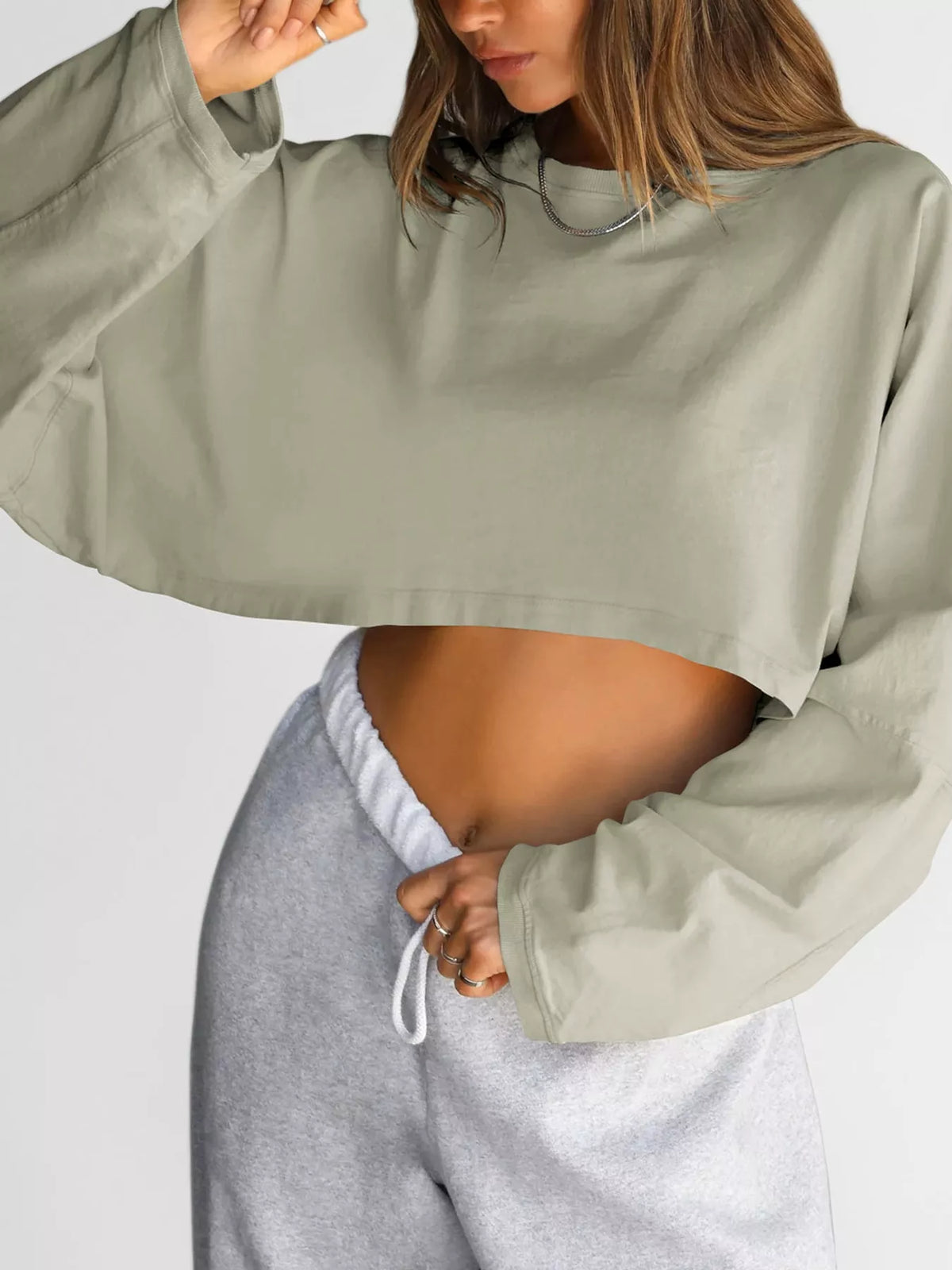 Close front view of a pale sage cropped sweatshirt worn with gray sweatpants.