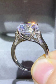 Side view of the round solitaire ring held between fingers, showing its raised setting.