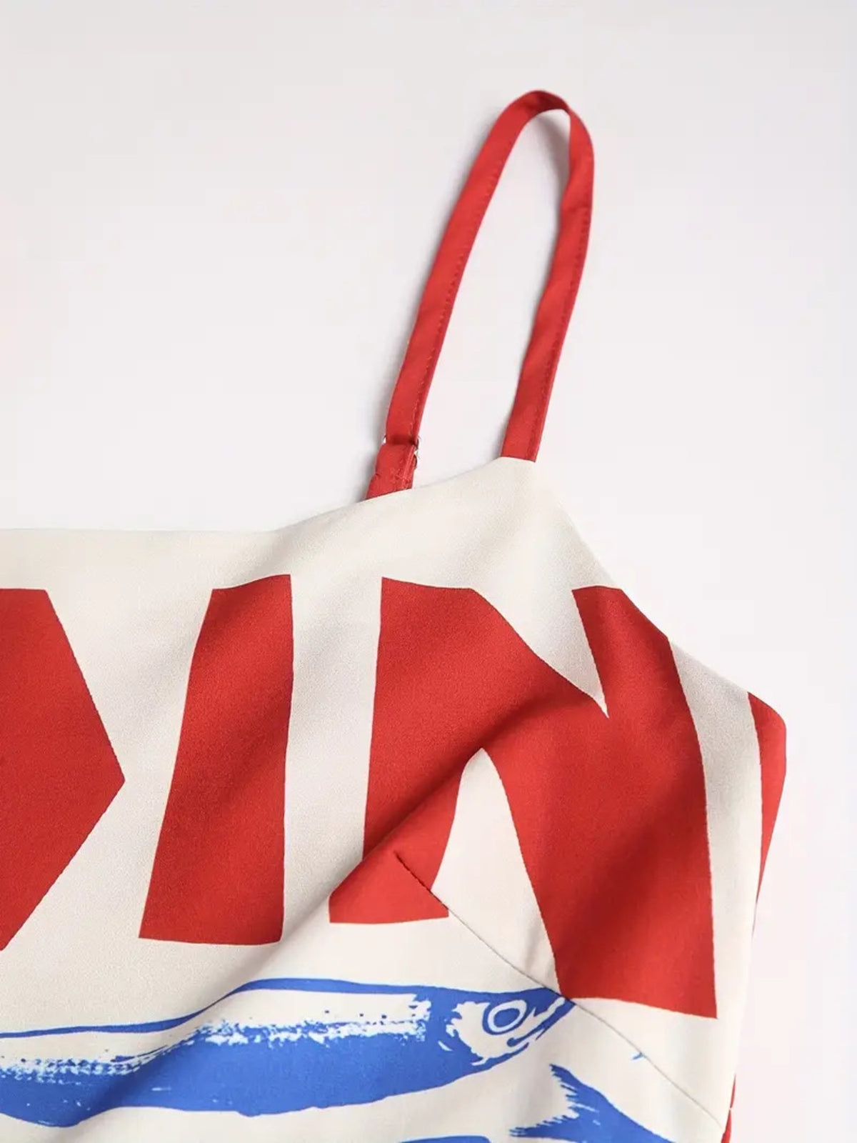Close-up of a red spaghetti strap and large red lettering on the white dress bodice.