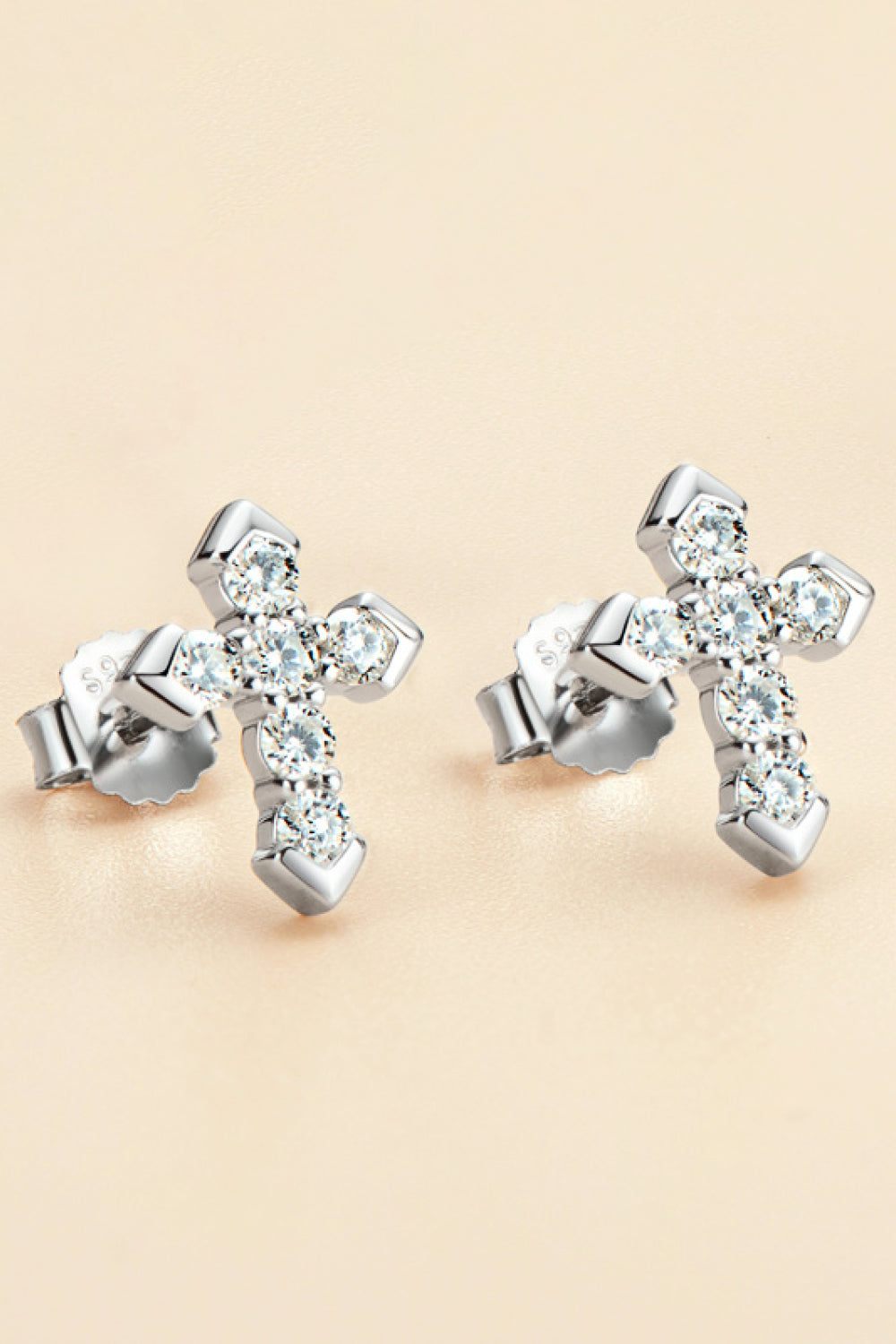 Pair of sparkling cross-shaped stud earrings arranged on a warm beige background