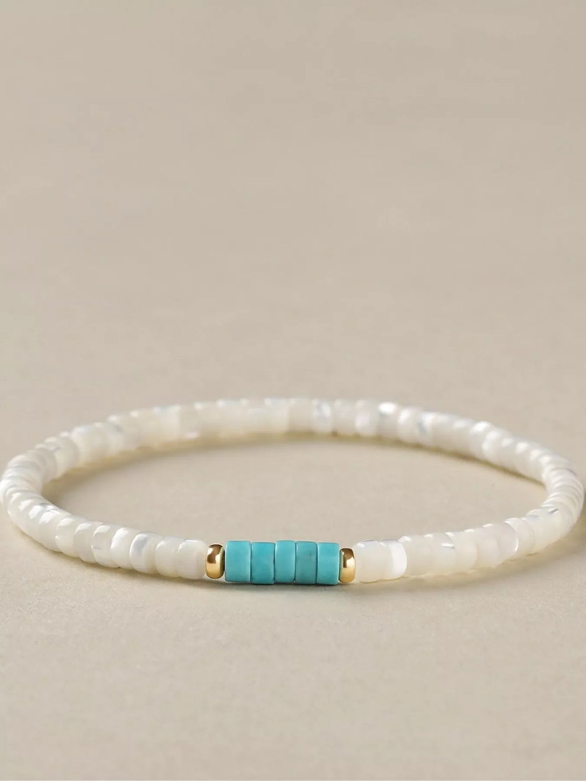 Side view of the turquoise accent beads and gold-tone spacers on a white bracelet