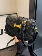 Black patterned flap crossbody bag held to show gold-coloured clasp and adjustable strap