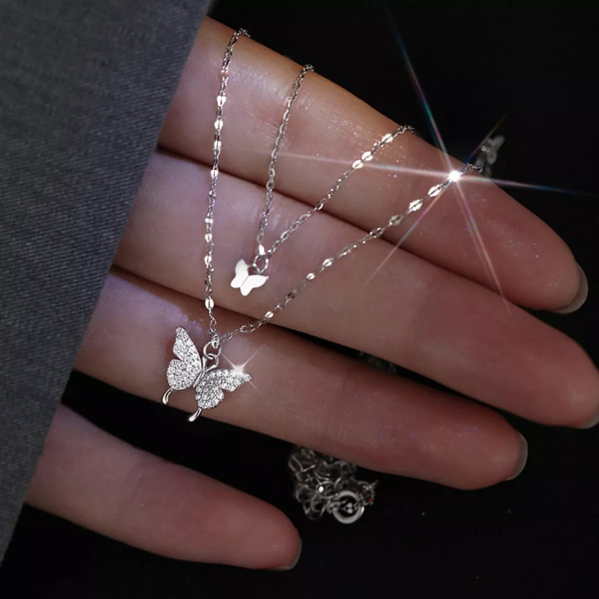 Two fine necklace chains with butterfly charms displayed across a hand