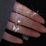 Two fine necklace chains with butterfly charms displayed across a hand