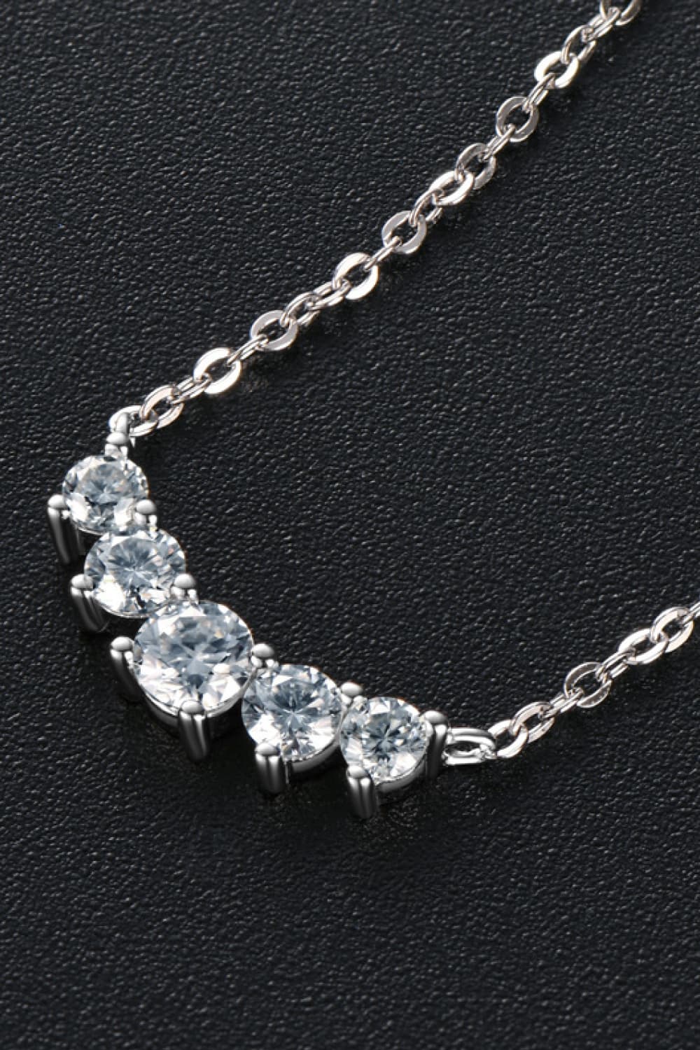 Close-up of clear stones along curved silver necklace on black background