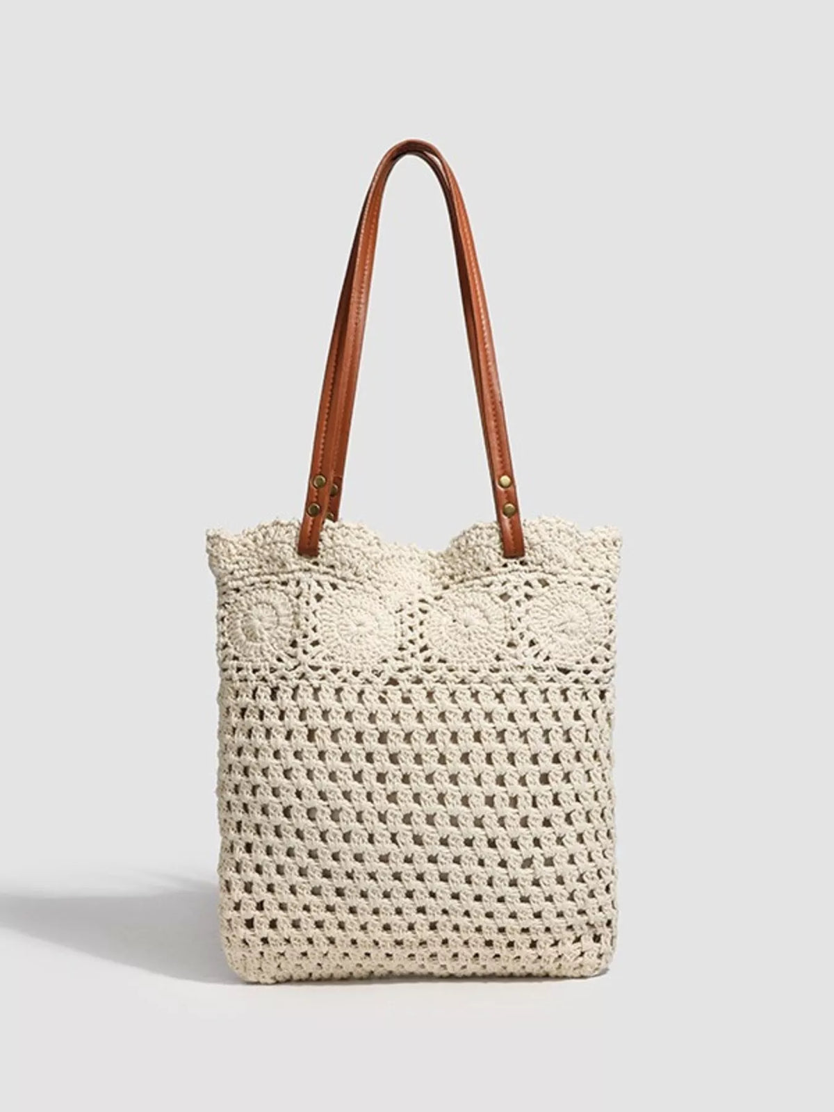 Ivory crochet tote with long brown handles and floral openwork motifs along the upper edge.