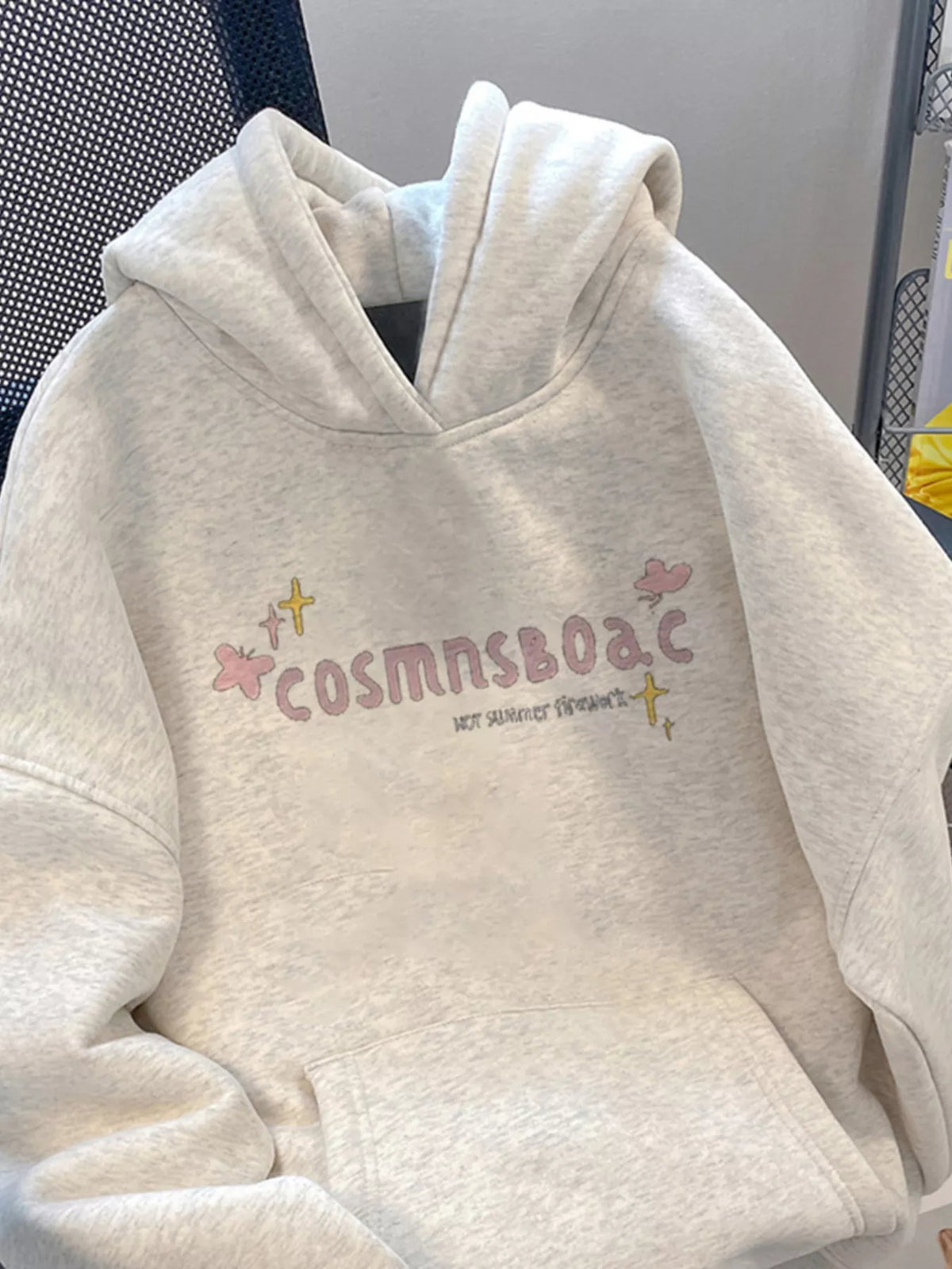 Front of light grey hoodie on a chair with pastel lettering and kangaroo pocket