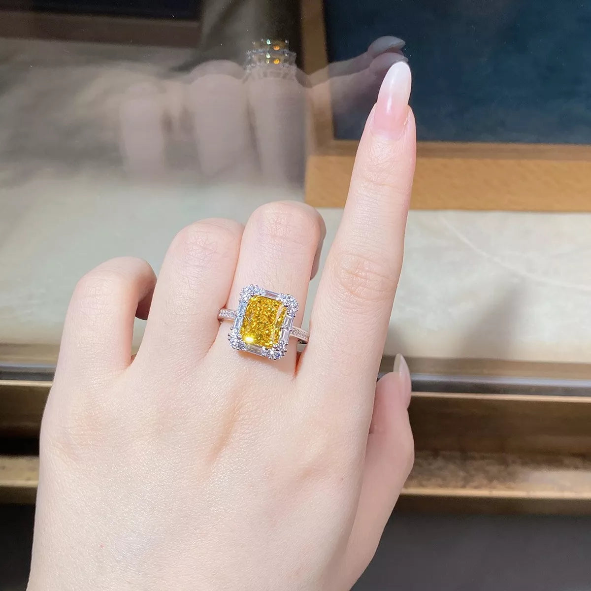 Rectangular yellow center stone ring with a clear-stone border worn on a hand
