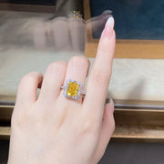 Rectangular yellow center stone ring with a clear-stone border worn on a hand