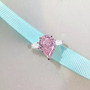 Two silver-tone teardrop rings shown with yellow and pink center stones.
