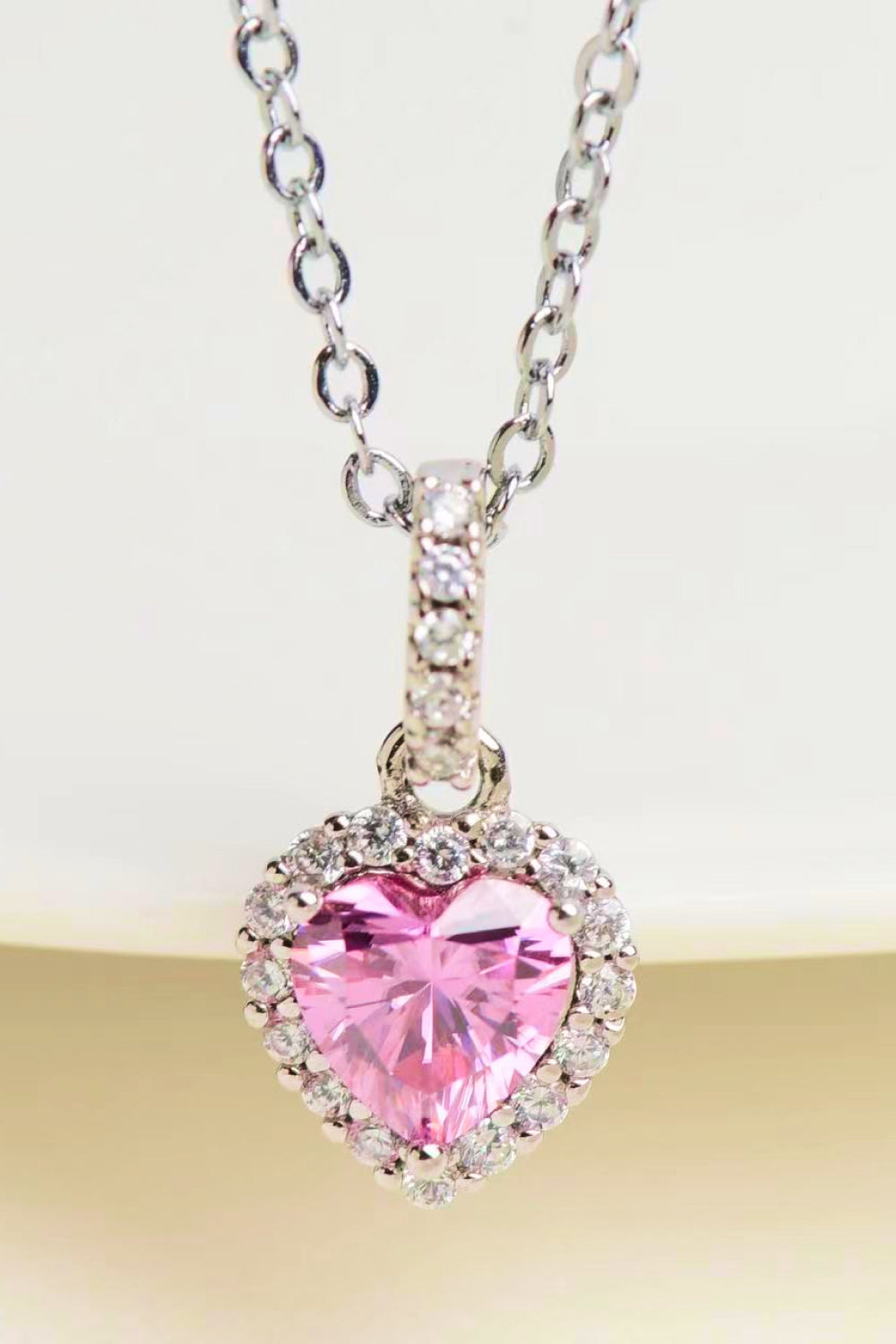 Pink heart-cut moissanite pendant with halo displayed on a tabletop