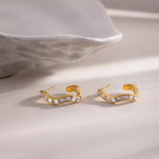 Pair of gold-tone zircon hoop earrings shown flat on a pale surface