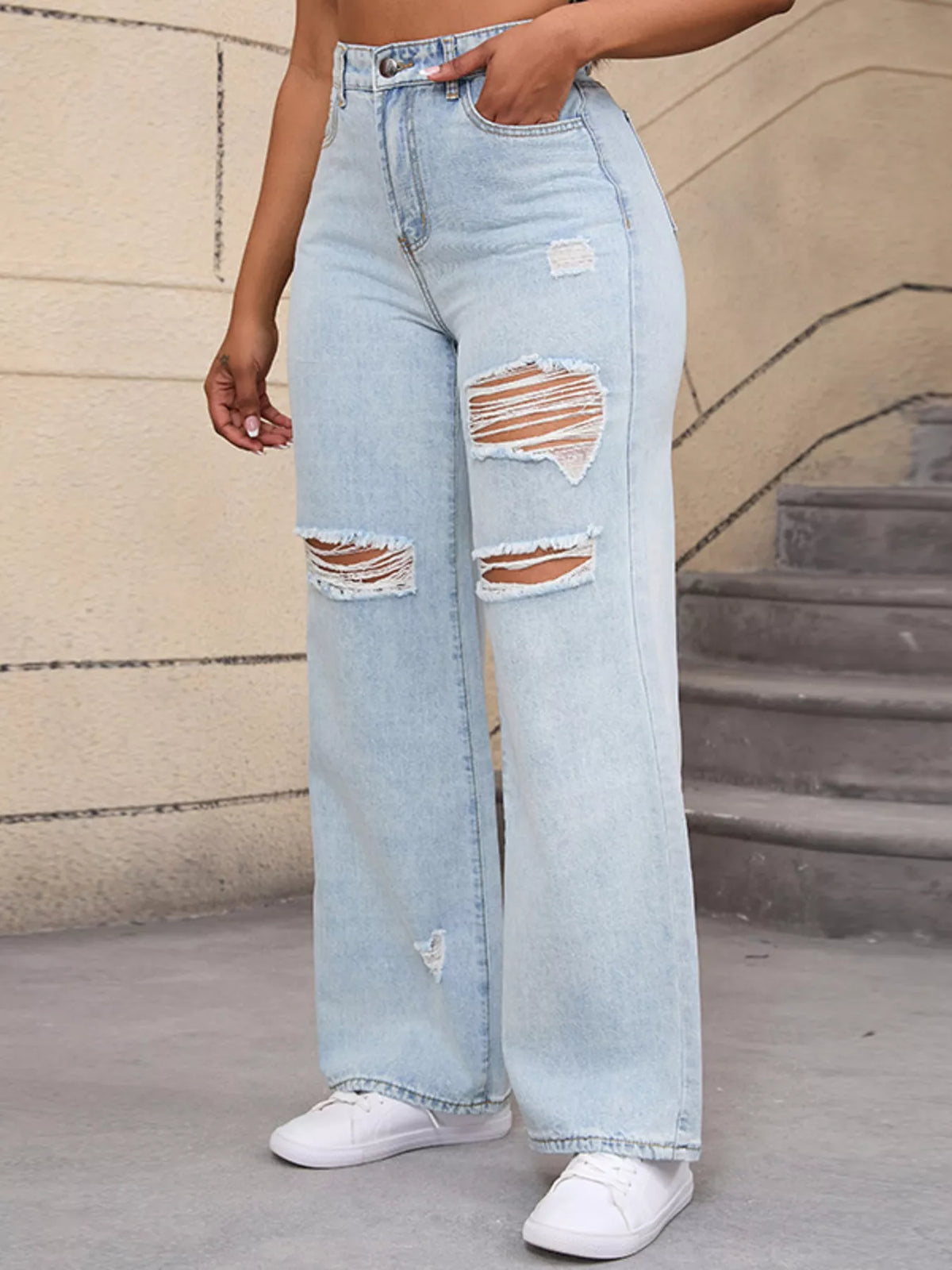 Three-quarter view of pale blue ripped jeans with a hand tucked in the front pocket