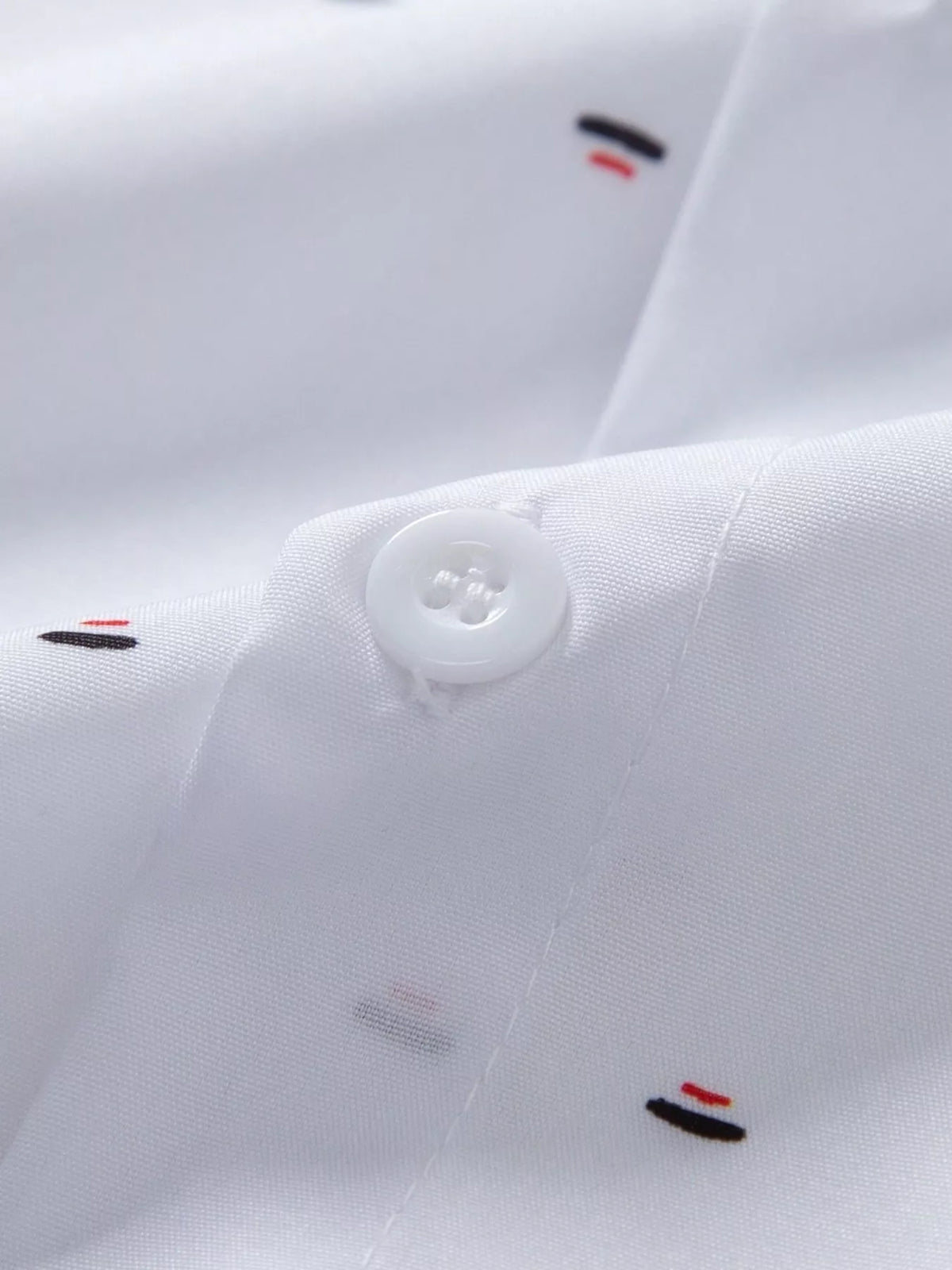 Close-up of white shirt fabric showing a button and small red and black printed motifs