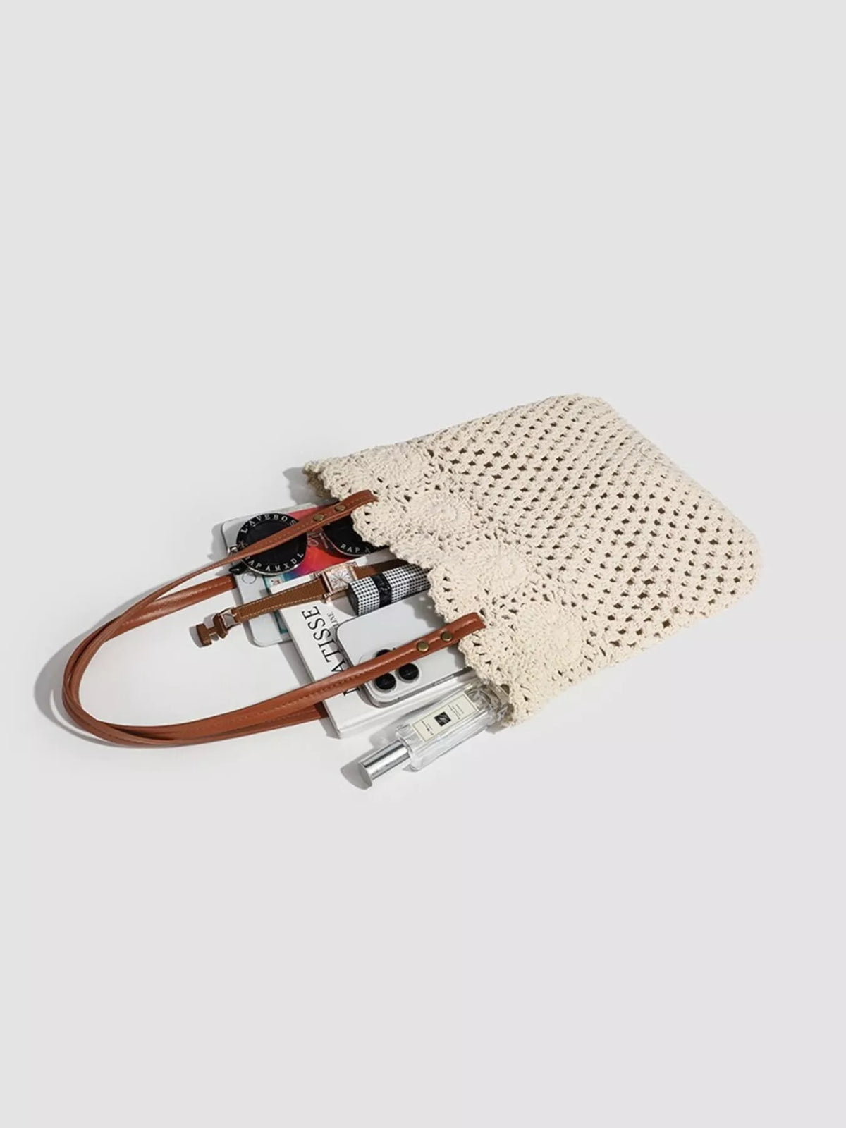 Ivory crochet tote lying flat with its brown handles beside small items shown for scale.