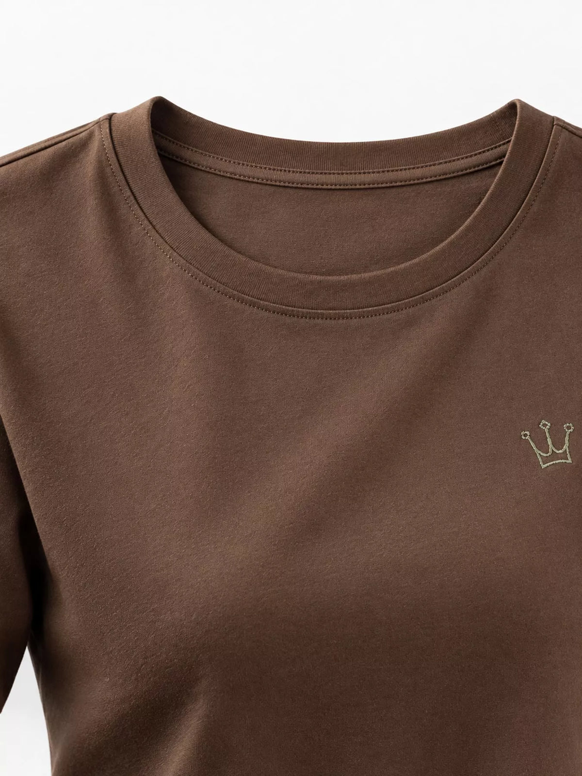 Close-up of brown T-shirt crew neckline and small crown emblem.