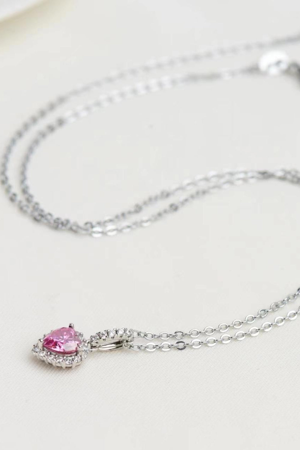 Silver-tone chain and pink heart pendant arranged on white surface