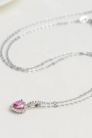 Silver-tone chain and pink heart pendant arranged on white surface