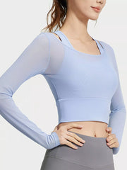 Angled view of light blue active top showing long sleeves and wide underbust band with hands on hips