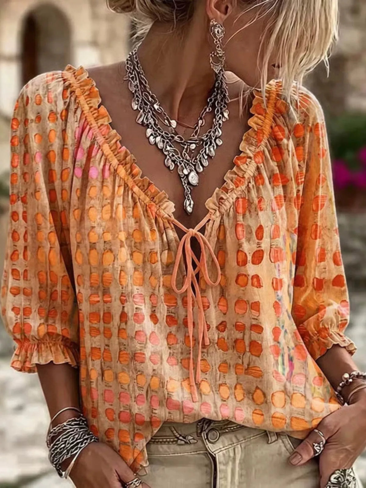 Model wearing an orange blouse with multicoloured spots, ruffled tie neckline and three-quarter sleeves