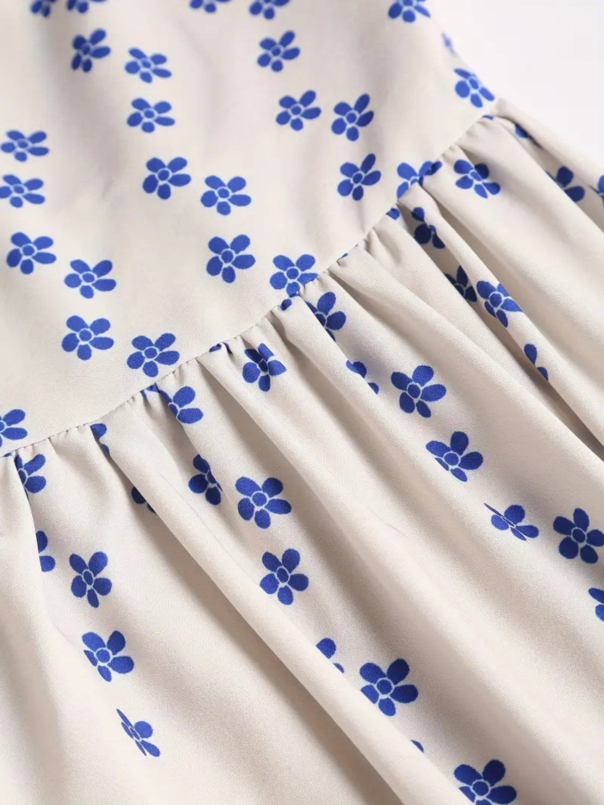 Close-up of small blue flowers and gathering at the waist seam of a white dress.