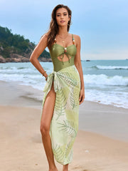 Light green cutout swimsuit with pale botanical sarong, full-length beach view