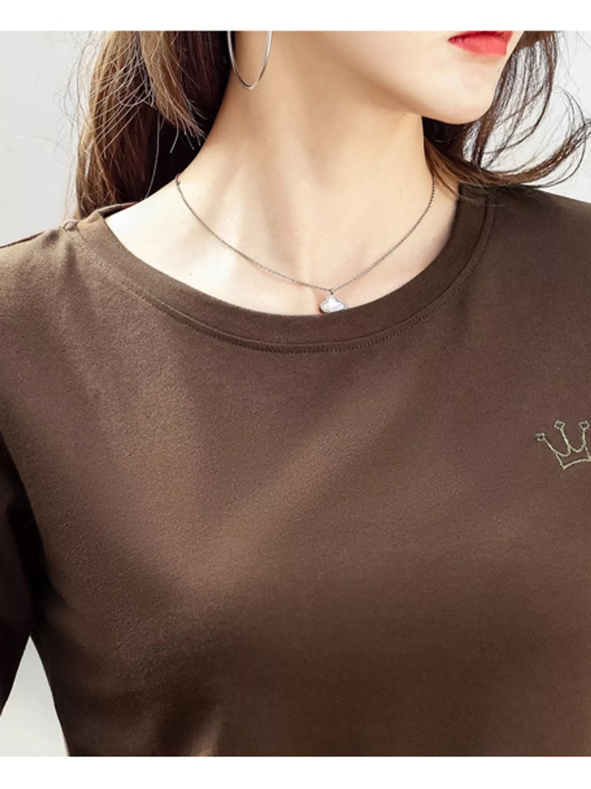 Close-up of brown T-shirt neckline and small crown emblem.