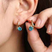 Gold-tone hoop earrings with purple stones shown close up on an ear