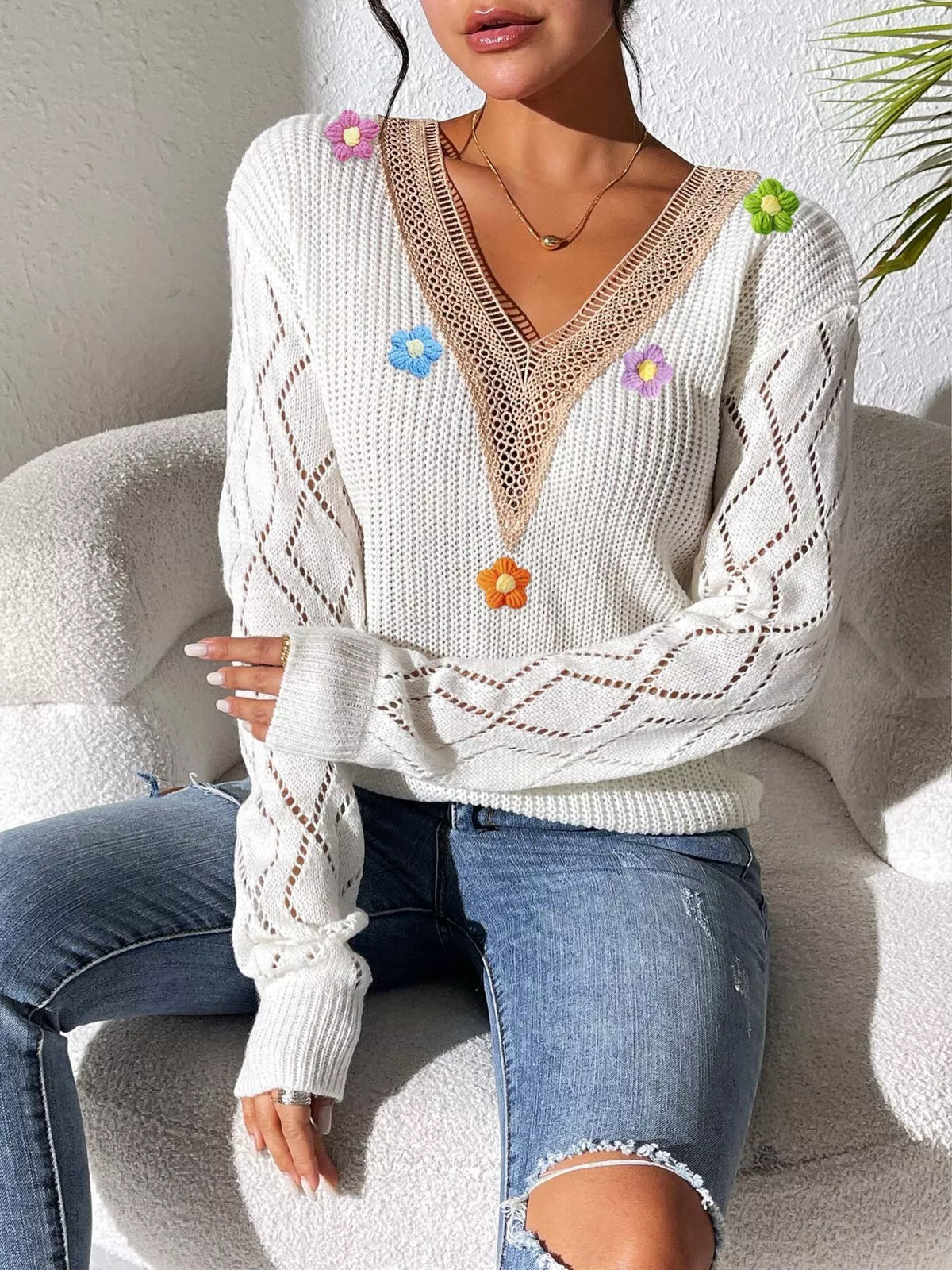 Seated view of the white floral-appliqué sweater, showing diamond openwork sleeves.